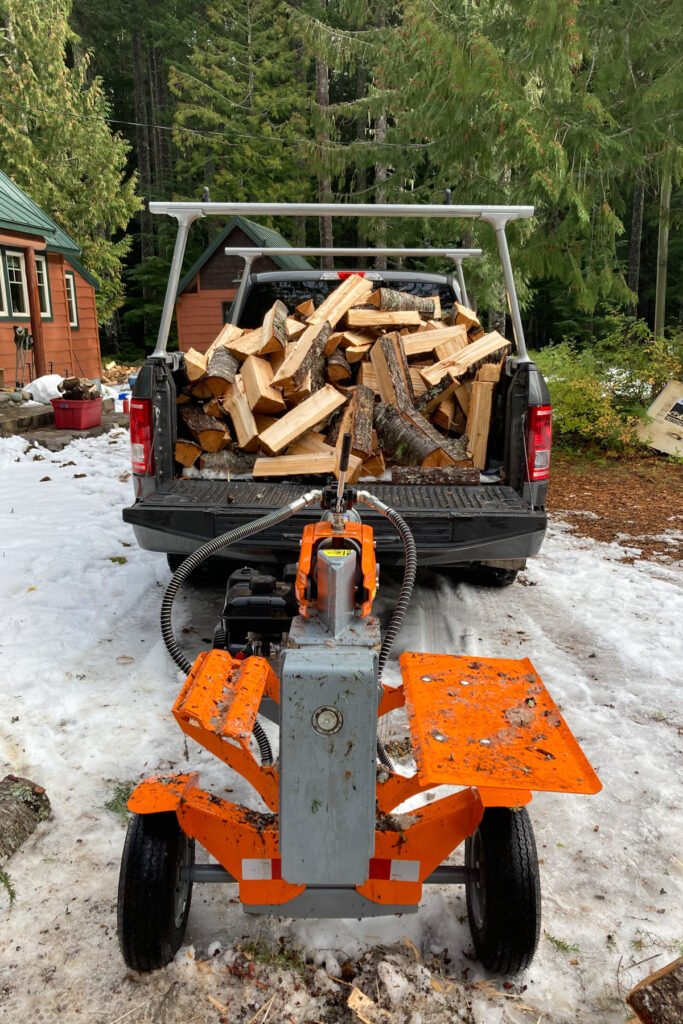 A ford pickup filled with cut firewood and a Yardmax log splitter hitched to the back.