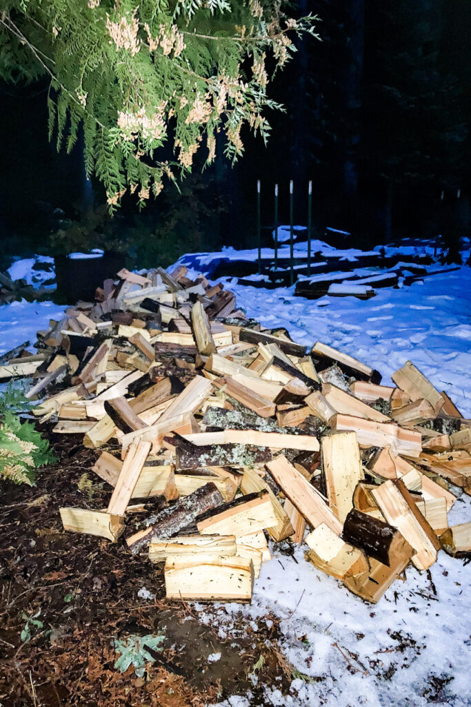 A large pile of chopped firewood outside on the snowy ground.