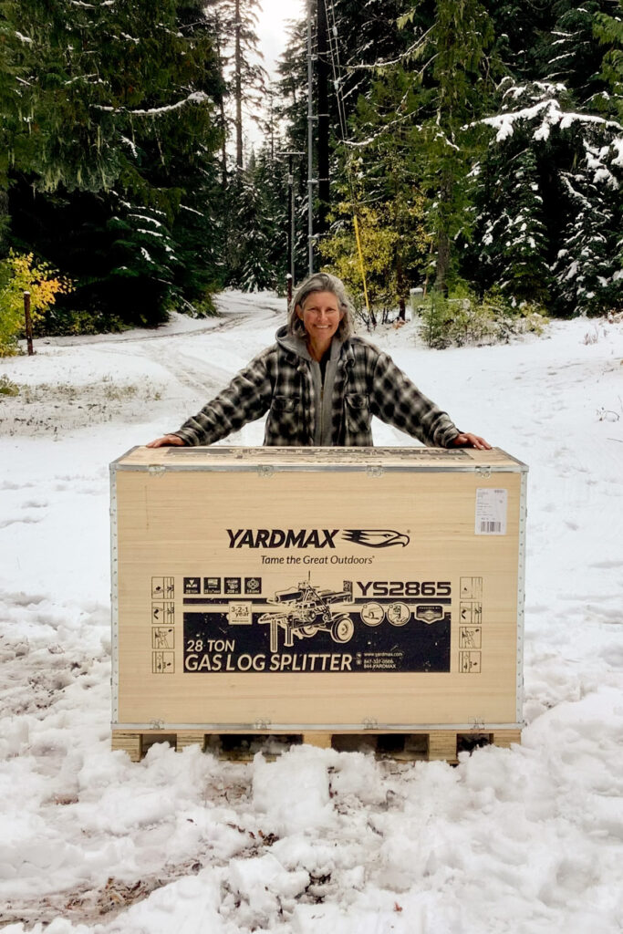 A woman standing in a snowy forest with a Yardmax Log Splitter in a shipping box.