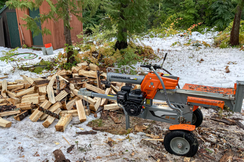 A yardmax 28 ton log splitter next to a pile of wood. There is snow on the ground.