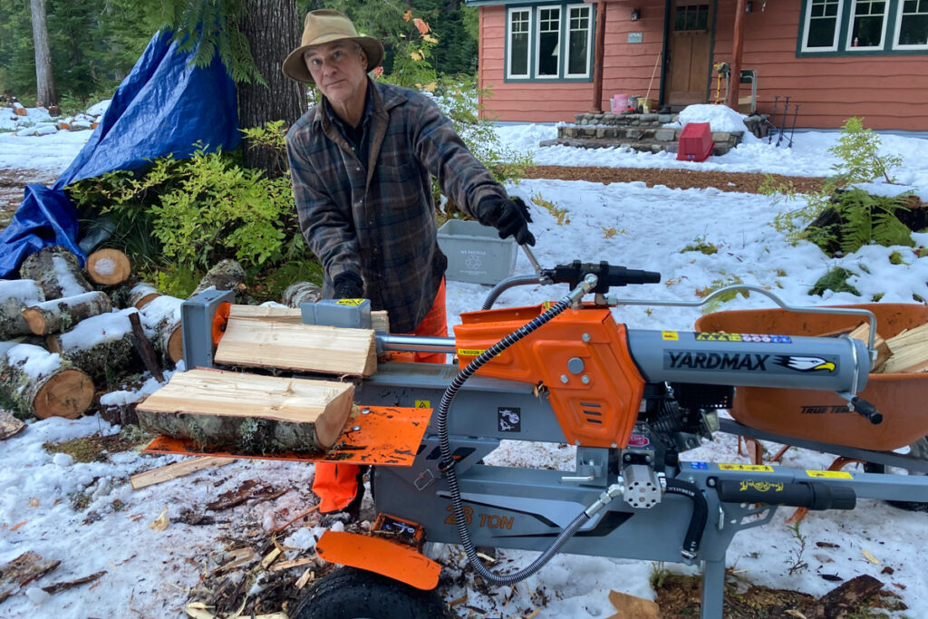Man in front of a cabin with snow on the ground. He is using a Yardmax log splitter.