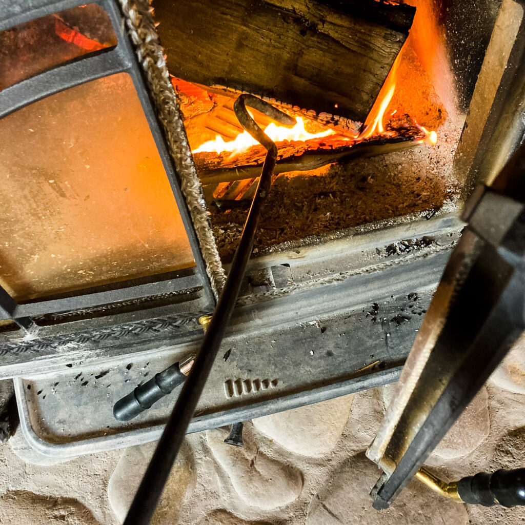 Forged steel fire poker inside a wood stove with a fire.