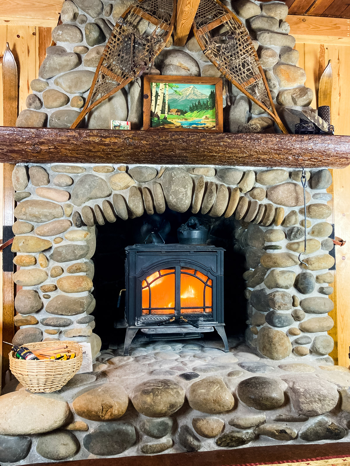 River rock fireplace with wood burning stove inset. A fire is burning in the stove.